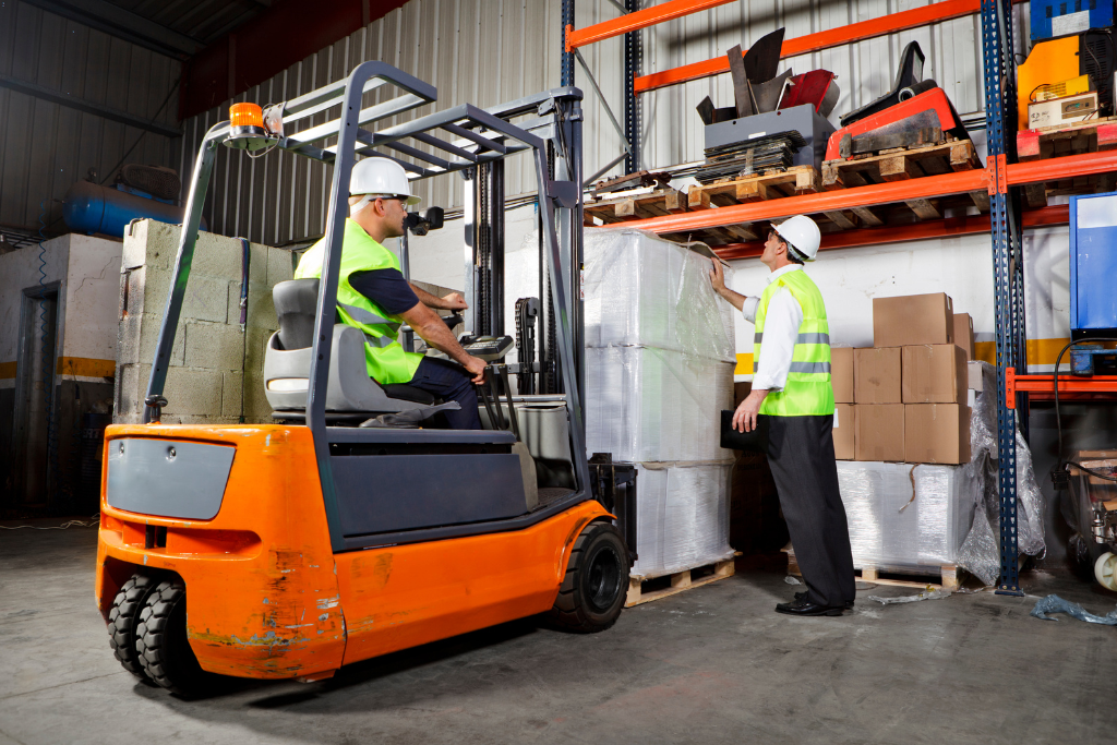 A forklift operator transports goods while a supervisor inspects items on a shelf