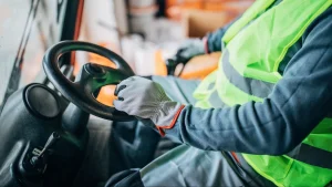 A worker in a reflective vest grips the steering wheel of a vehicle